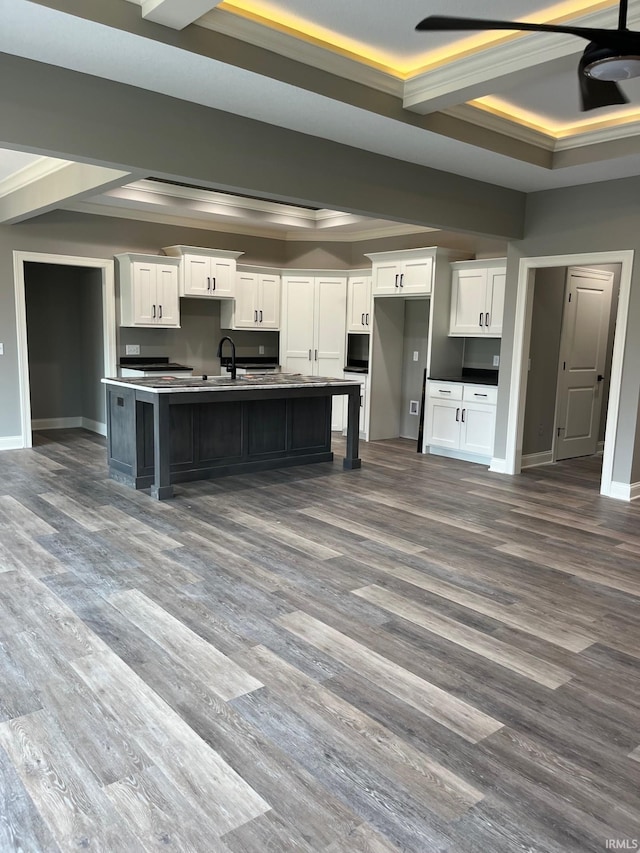 kitchen with hardwood / wood-style flooring, white cabinetry, a kitchen island with sink, and ornamental molding