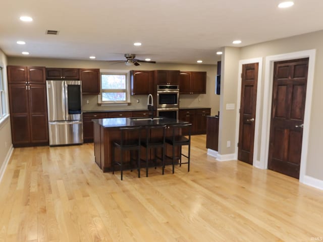 kitchen with appliances with stainless steel finishes, a kitchen island with sink, sink, light hardwood / wood-style flooring, and a breakfast bar area