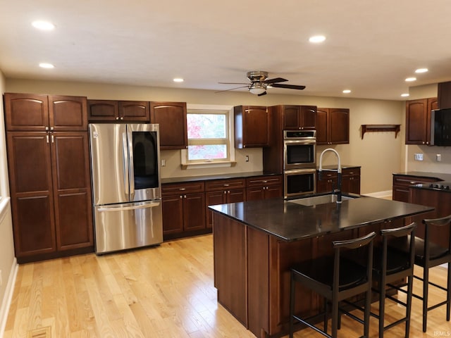 kitchen featuring a center island with sink, a kitchen bar, light wood-type flooring, and appliances with stainless steel finishes