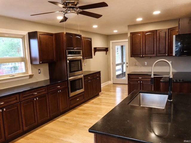 kitchen featuring light wood-type flooring, dark brown cabinets, stainless steel double oven, ceiling fan, and sink