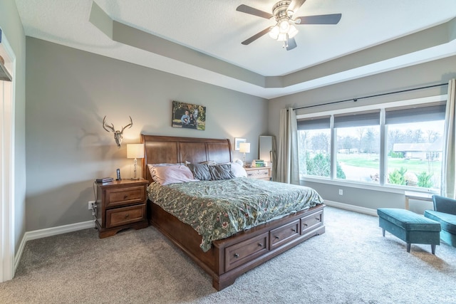 bedroom featuring a textured ceiling, light colored carpet, ceiling fan, and a tray ceiling