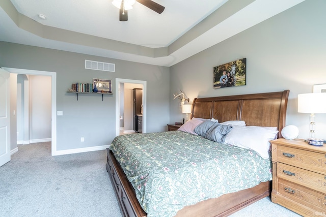 carpeted bedroom featuring connected bathroom, a tray ceiling, and ceiling fan