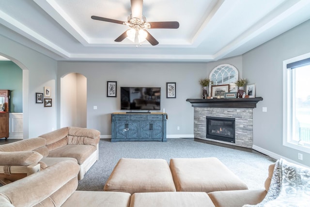 carpeted living room with ceiling fan, a healthy amount of sunlight, a raised ceiling, and a fireplace