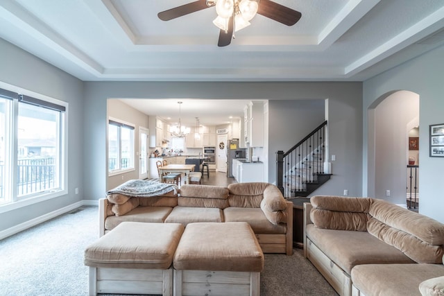 carpeted living room with ceiling fan with notable chandelier and a tray ceiling