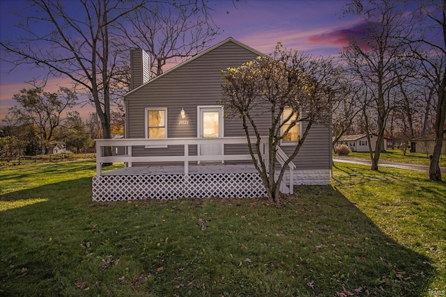 back house at dusk featuring a lawn and a wooden deck