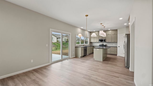 kitchen with sink, light wood-type flooring, appliances with stainless steel finishes, decorative light fixtures, and a kitchen island