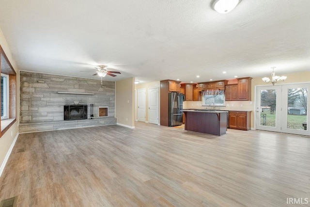 kitchen with stainless steel refrigerator, a center island, light hardwood / wood-style flooring, pendant lighting, and a fireplace