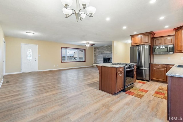 kitchen featuring pendant lighting, ceiling fan with notable chandelier, light wood-type flooring, appliances with stainless steel finishes, and light stone counters