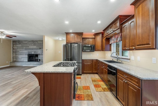 kitchen with light wood-type flooring, stainless steel appliances, a kitchen island, sink, and a stone fireplace