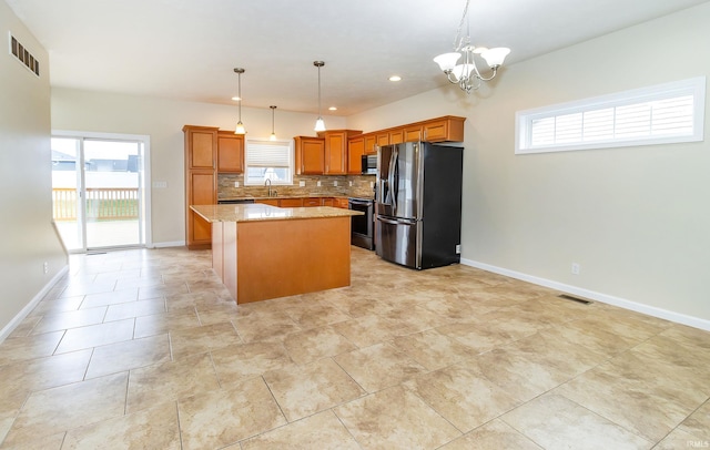 kitchen with backsplash, an inviting chandelier, hanging light fixtures, appliances with stainless steel finishes, and a kitchen island