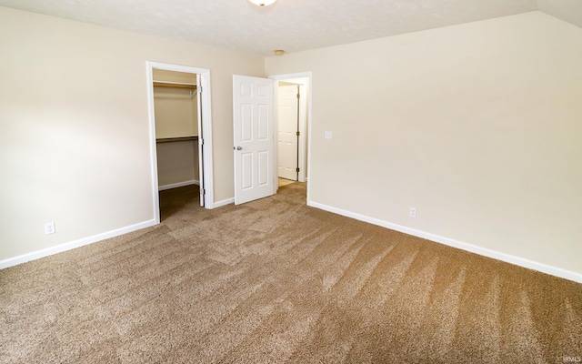 unfurnished bedroom featuring carpet flooring, a spacious closet, a closet, and vaulted ceiling