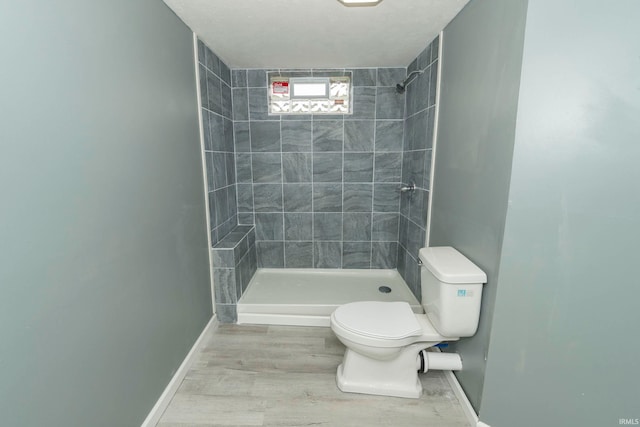 bathroom with hardwood / wood-style floors, a tile shower, and toilet