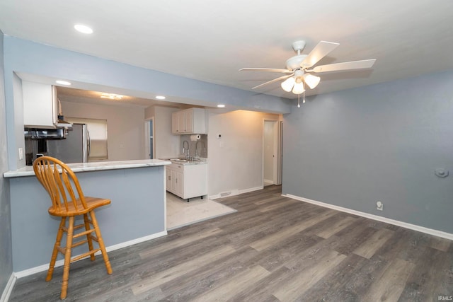 kitchen featuring a kitchen bar, kitchen peninsula, sink, white cabinets, and dark hardwood / wood-style floors