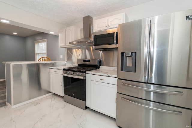 kitchen featuring wall chimney exhaust hood, stainless steel appliances, light stone counters, kitchen peninsula, and white cabinets