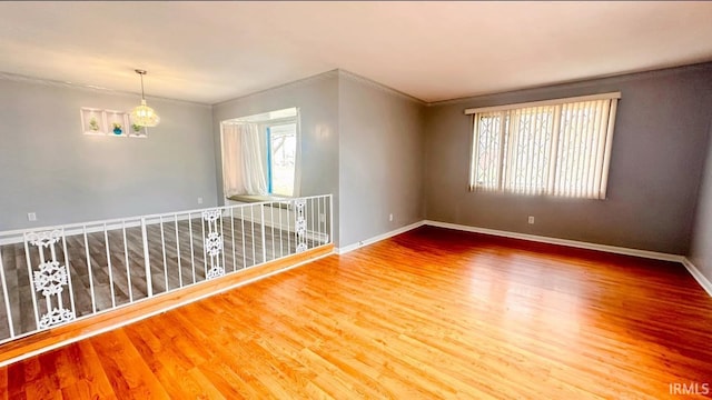 empty room featuring hardwood / wood-style floors, a notable chandelier, and ornamental molding