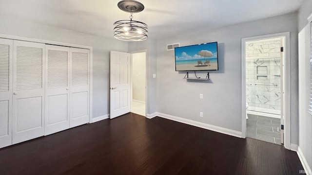 unfurnished bedroom with ensuite bathroom, dark wood-type flooring, and a chandelier