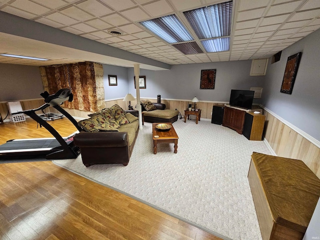 living room featuring wooden walls, a drop ceiling, and wood-type flooring