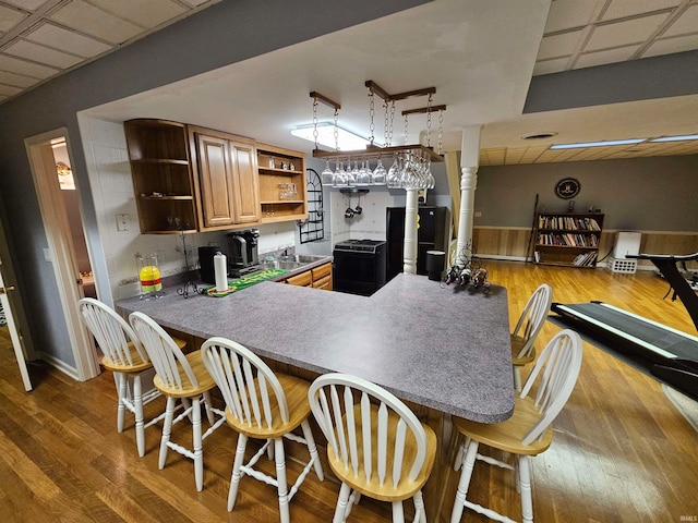 kitchen with kitchen peninsula, hardwood / wood-style flooring, a breakfast bar area, and black appliances