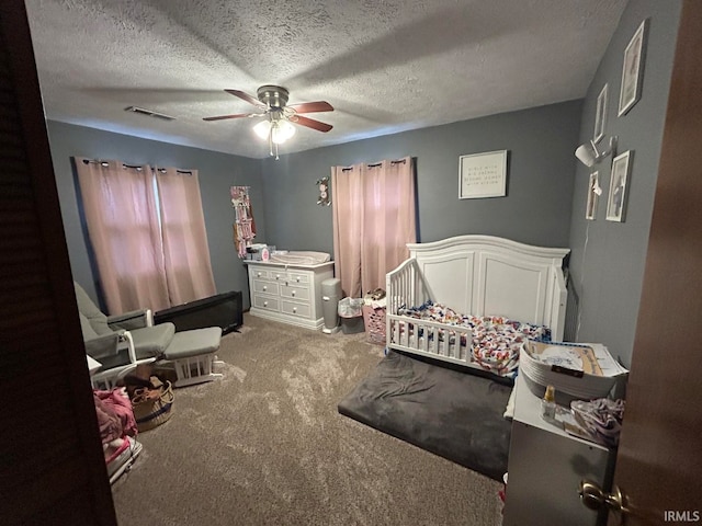 carpeted bedroom featuring ceiling fan, a crib, and a textured ceiling