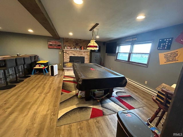 playroom featuring hardwood / wood-style floors, billiards, a brick fireplace, baseboard heating, and beamed ceiling