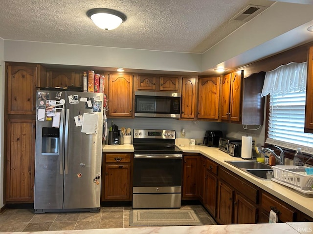 kitchen with a textured ceiling, light tile patterned floors, sink, and appliances with stainless steel finishes