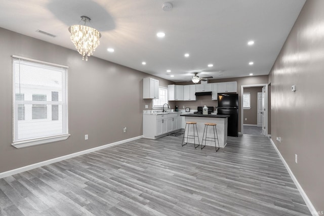 kitchen featuring a breakfast bar, black fridge, hanging light fixtures, light wood-type flooring, and a kitchen island