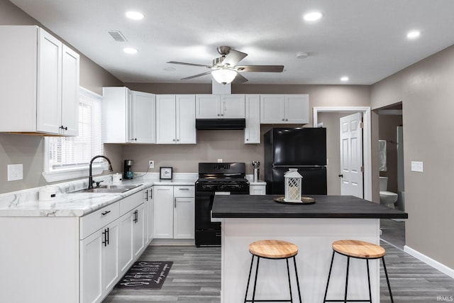 kitchen featuring a kitchen breakfast bar, sink, black appliances, a center island, and white cabinetry