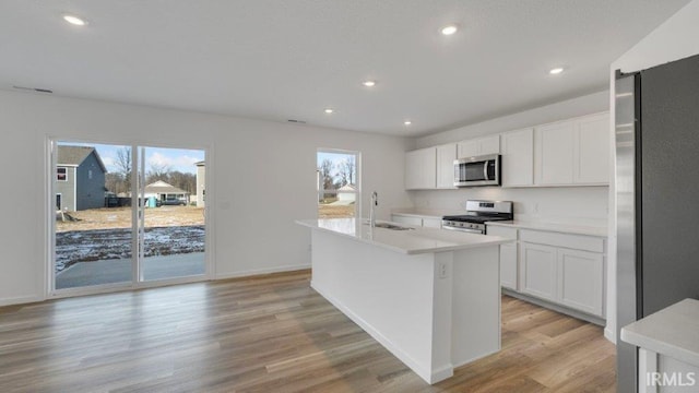 kitchen with white cabinets, sink, light hardwood / wood-style flooring, an island with sink, and appliances with stainless steel finishes