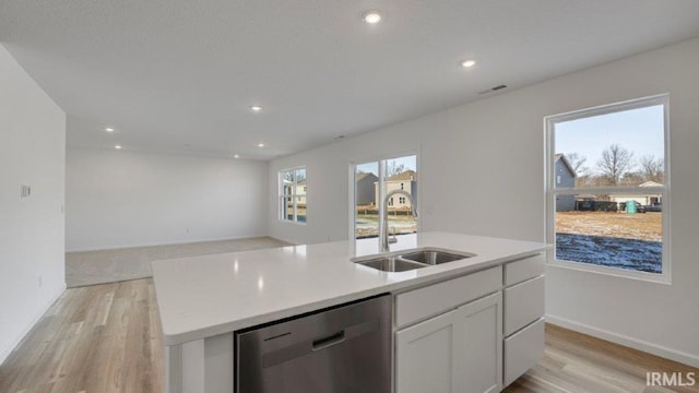 kitchen with light wood-type flooring, white cabinets, sink, dishwasher, and an island with sink