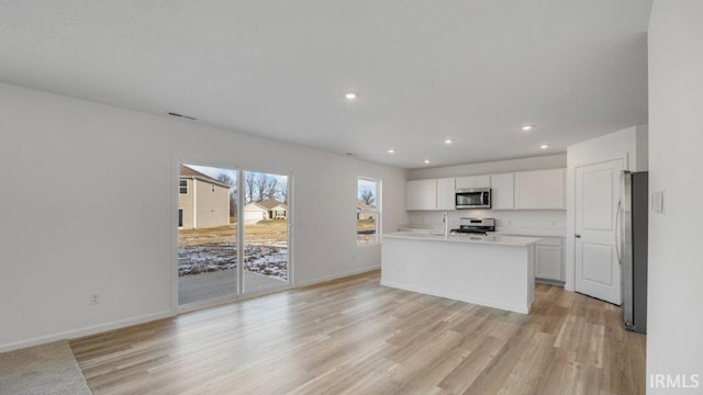 kitchen with sink, light wood-type flooring, an island with sink, white cabinetry, and stainless steel appliances