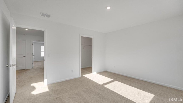 unfurnished bedroom featuring a walk in closet, a closet, and light colored carpet