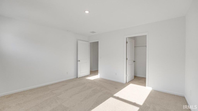 unfurnished bedroom featuring light carpet, a walk in closet, and a closet