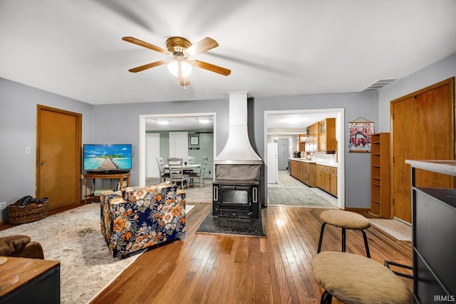 living room featuring ceiling fan, light hardwood / wood-style floors, and a wood stove