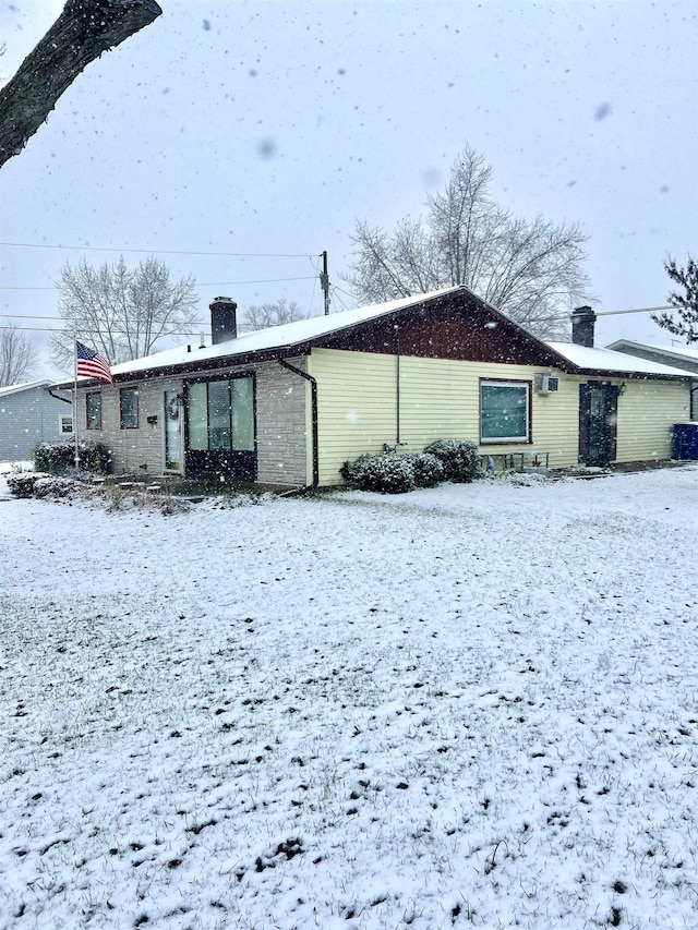 snow covered rear of property featuring a wall unit AC