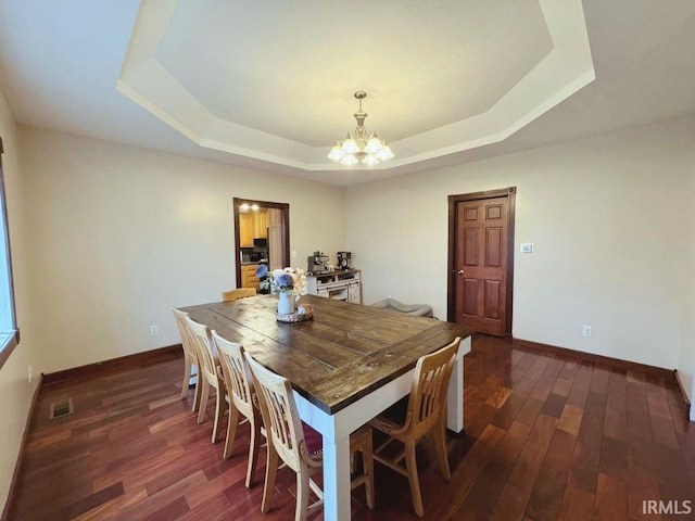 dining space with dark wood-type flooring, a tray ceiling, and a chandelier