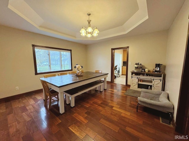 dining space featuring a tray ceiling, dark wood-type flooring, and a notable chandelier