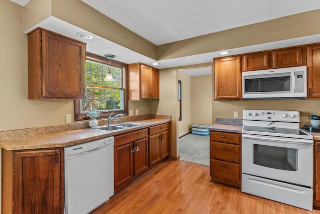 kitchen with decorative light fixtures, white appliances, sink, and light hardwood / wood-style flooring