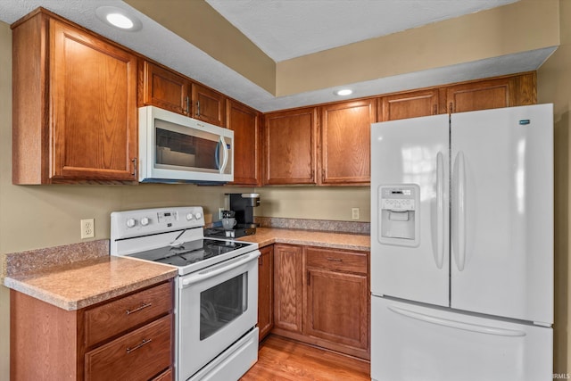 kitchen featuring a textured ceiling, white appliances, and light hardwood / wood-style floors