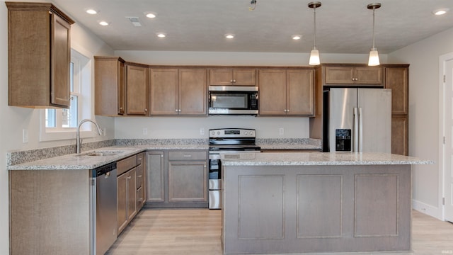 kitchen featuring stainless steel appliances, a kitchen island, light hardwood / wood-style flooring, light stone counters, and sink