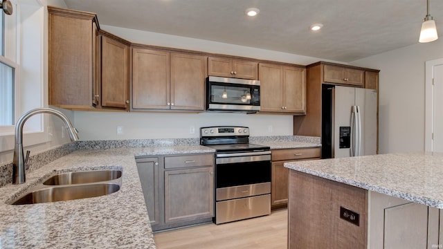 kitchen with light stone countertops, decorative light fixtures, stainless steel appliances, sink, and light wood-type flooring