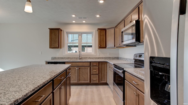 kitchen with light stone counters, sink, appliances with stainless steel finishes, and light hardwood / wood-style flooring