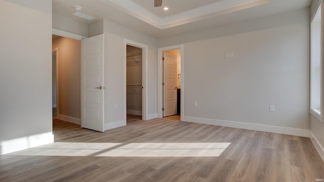 unfurnished bedroom featuring a raised ceiling, light wood-type flooring, a closet, ornamental molding, and a walk in closet