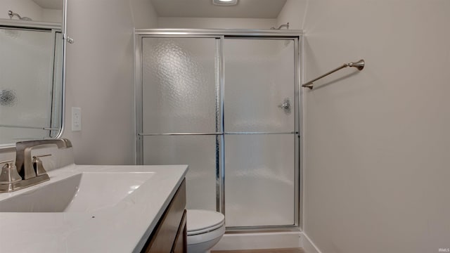 bathroom featuring a shower with shower door, toilet, and vanity