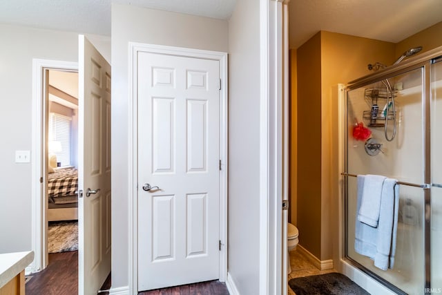 bathroom featuring hardwood / wood-style floors, toilet, a shower with door, and a textured ceiling