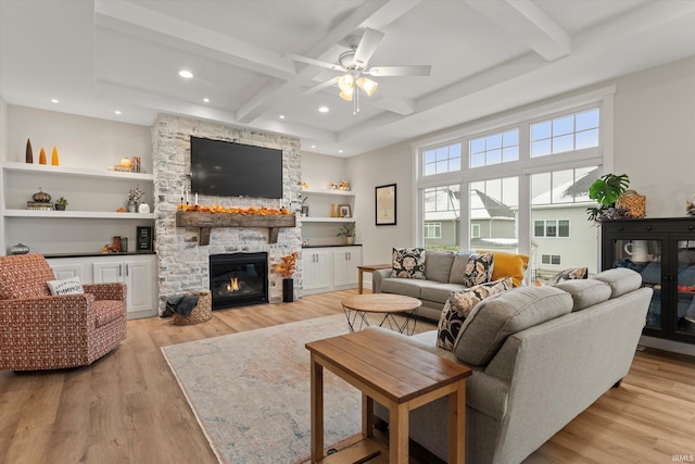 living room with a stone fireplace, ceiling fan, built in features, beamed ceiling, and light hardwood / wood-style floors