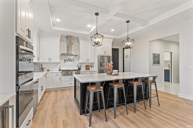 kitchen with white cabinetry, a center island, wall chimney exhaust hood, stainless steel appliances, and light hardwood / wood-style floors