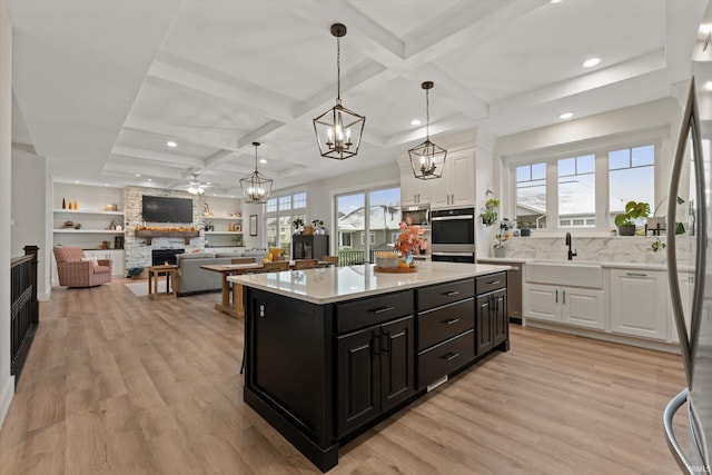 kitchen featuring a stone fireplace, white cabinetry, light wood-type flooring, and a wealth of natural light