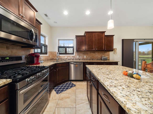 kitchen with light stone countertops, sink, hanging light fixtures, stainless steel appliances, and backsplash