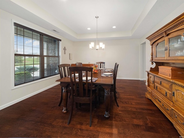 dining space featuring a raised ceiling, dark wood-type flooring, and an inviting chandelier