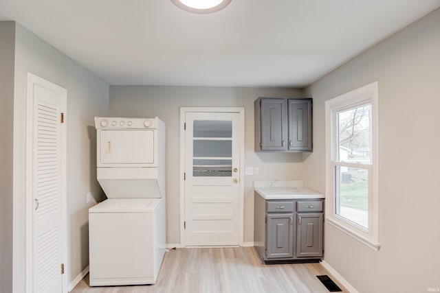 clothes washing area featuring cabinets, stacked washing maching and dryer, light hardwood / wood-style flooring, and a healthy amount of sunlight